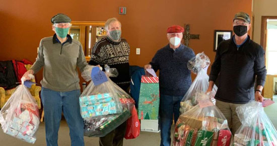 Volunteers from the Holiday Baskets Program hold up bags of donated gifts