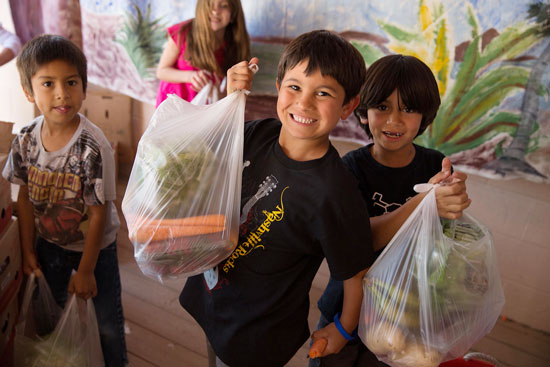 Totes of Hope® recipients hold up bags of fresh produce they received. 